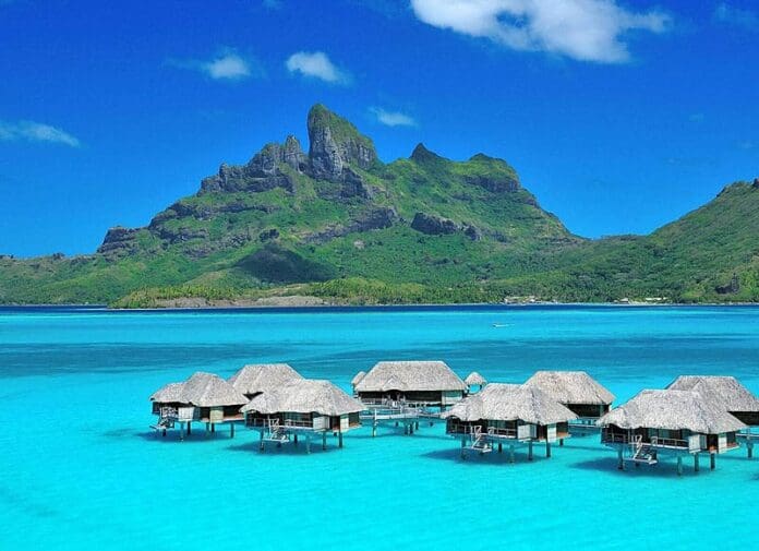 A group of thatched roof huts in the middle of an ocean.